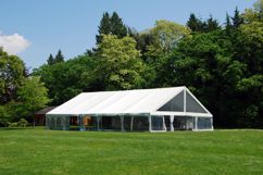 Green space with trees in the back ground and a wedding tent/special event tent set up.